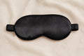 Masque de sommeil en soie naturelle noir poudré YaNa Confort posé sur tissu beige