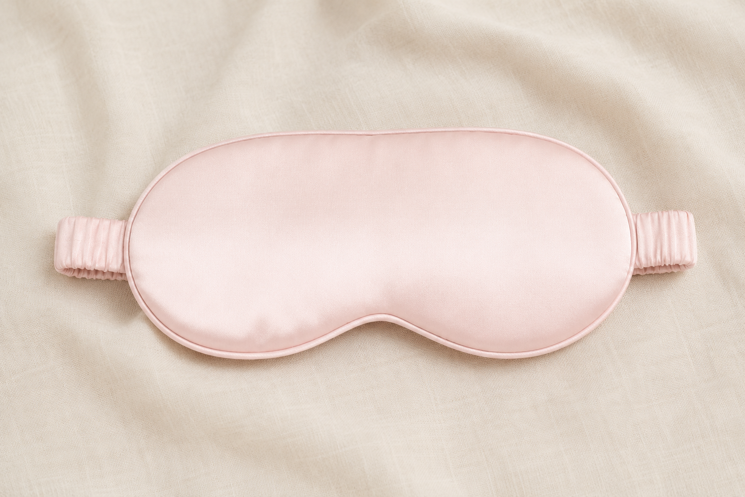 Masque de sommeil en soie naturelle rose poudré YaNa Confort posé sur tissu beige